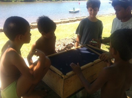 Crianças livres jogando uma sinuca improvisada em um caixote com bolinhas de gude a margem do rio